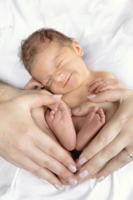 photo d'un bébé nouveau né souriant dans les bras de ses parents, mains en forme de coeur et petit pied de bébé sur fond blanc