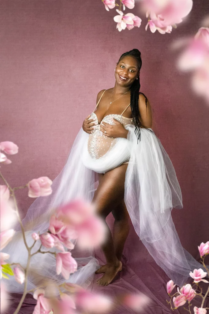 Photo artistique de photographe d'une femme enceinte, future maman qui attends un bébé de profil tenant son ventre, nu artistique couverte d'un voilage en tulle blanc avec un reflet d'eau