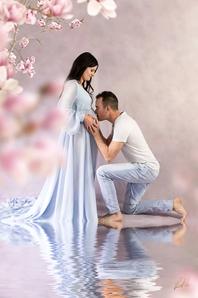 Photo artistique de photographe d'une femme enceinte, future maman qui attends un bébé de profil tenant son ventre, nu artistique couverte d'un voilage en tulle blanc avec un reflet d'eau