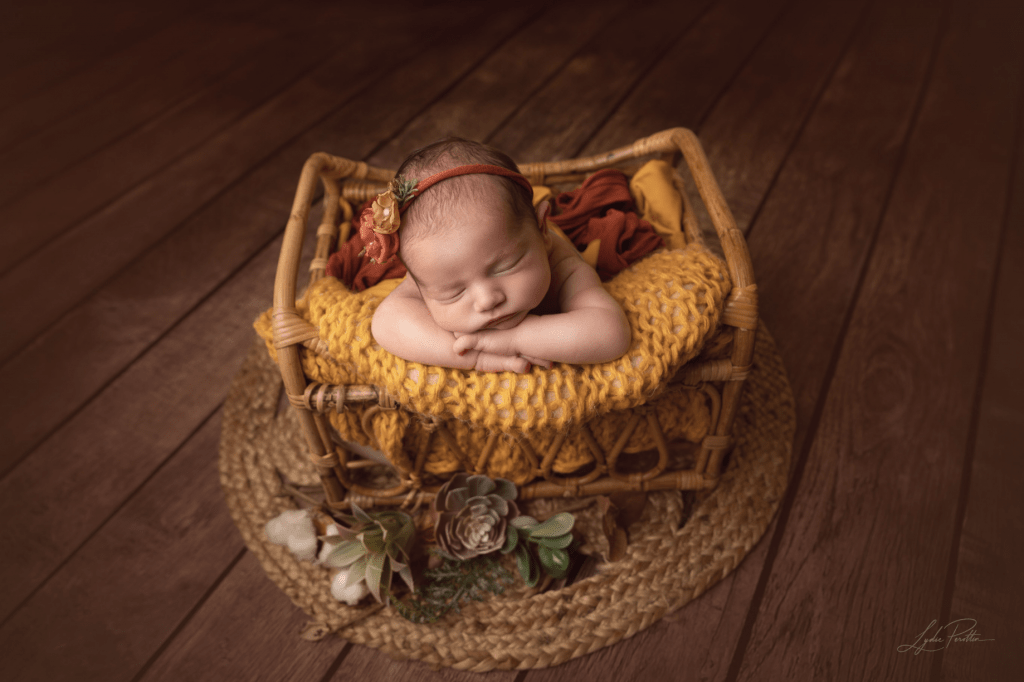 Photograhie bébé nouveau né fille dans un contenant en bois rotin sur une couverture toute douce orange et terra cotta